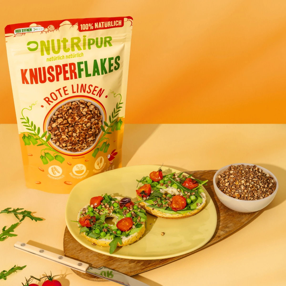 Billedet viser røde sprøde linsflager som topping på en bagel