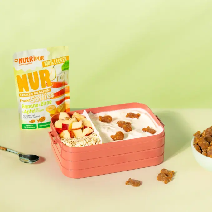 Billedet viser det bløde frugtslik “Softies” med banan, pære og æble med crispies som skolesnack i en madkasse.