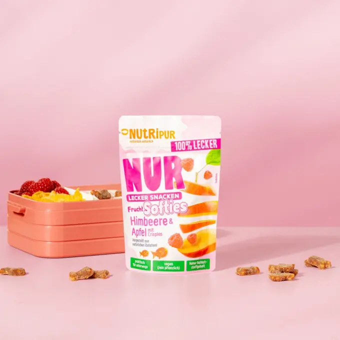Billedet viser det bløde frugtslik “Softies” med hindbær og æble med crispies med emballage og en madkasse.