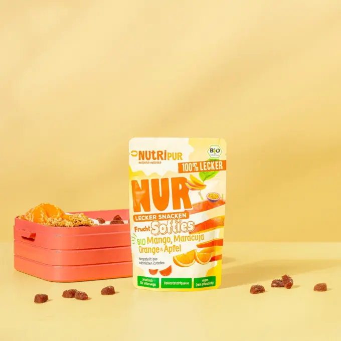 Billedet viser det økologiske bløde frugtslik “Softies” med mango, passionsfrugt, appelsin og æble med emballage og madkasse.